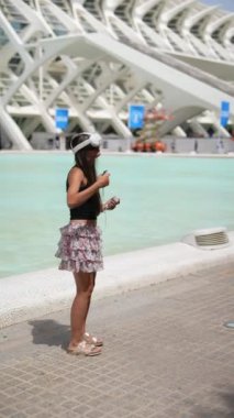 VR kulaklıklı genç bir kadın modern mimari yapı ve su yakınlarındaki sanal gerçeklikle etkileşime giriyor..