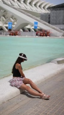 Genç bir kadın sanal gerçeklik deneyimi için sanal gerçeklik kulaklığı kullanarak havuz kenarında oturuyor.