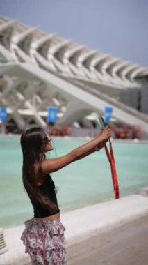 Fütürist mimari havuz başında şık giyinmiş bir kadın selfie çekiyor. Modern yaşam tarzını yakalar.