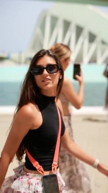 Siyah bluz, çiçek desenli etek ve güneş gözlüğü giyen şık genç bir kadın gelecekteki mimari yapının yanında yürüyor.