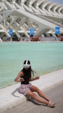 Bir kadın güneşli bir günde suyun yakınındaki fütüristik bir mimaride sanal gerçeklik deneyiminin tadını çıkarıyor.