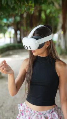 Genç bir kadın yeşil bir ortamda VR 'ı seviyor, gelişmiş teknolojiyi şık bir ortamda kucaklıyor.