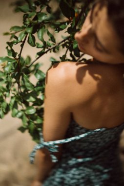 Çiçekli bir elbise giymiş bir kadın, güneş ışığında yeşilliğin yanında, kırsal ve huzurlu bir ortam yaratıyor, sanatsal, rüya gibi bir görüntü.