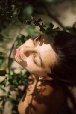 Huzurlu sahnede, bir kadın güneşin altında güneşleniyor canlı yeşil yaprakların arasında, ışıldayan güzellik ve sükunet.