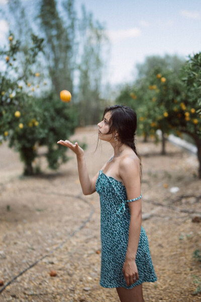 Woman Wearing Blue Dress Seen Tossing Orange Sunny Orchard Trees Stock Photo