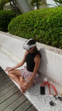 Huzurlu bir şekilde meditasyon yapan bir kadın, VR kulaklığı takıyor ve rahat bir şekilde bankta oturuyor.