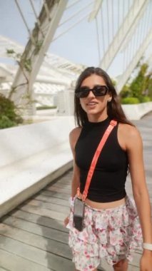 Siyah bluzlu ve çiçekli etekli mutlu bir kadın modern mimari bir mekanda günün tadını çıkarıyor..