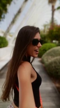 Uzun saçlı, siyah bluzlu ve çiçekli etekli bir kadın güneşli bir günün tadını çıkarıyor..