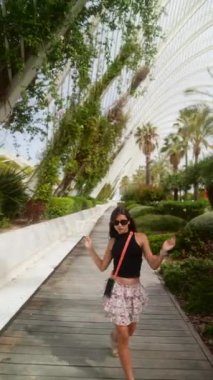 Bir kadın neşeyle gezer yemyeşil bir yolda, güneşli havanın ve güzel manzaranın tadını çıkararak.