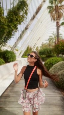 Siyah bluz ve çiçekli etek giyen neşeli bir kadın güneşli bir günde güzel bir botanik bahçesinde gezinir..