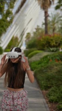 VR kulaklık takan bir kadın açık havada sanal gerçeklik deneyimi yaşayan palmiye ağaçlarıyla dolu yemyeşil bir bahçeye daldırılır.