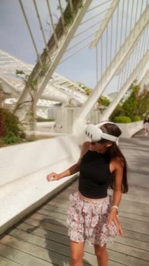 Güneşli, park benzeri bir ortamda sanal gerçeklik deneyimi yaşayan genç bir kadın..