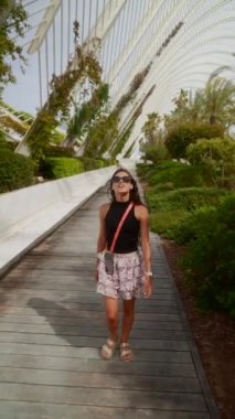 Moda güneş gözlüğü ve şık bir kıyafet takan şık genç bir kadın modern bir açık hava ortamında yürüyor.