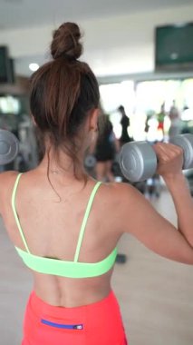 Genç bir kadın spor salonunda antrenman yapıyor. Halterli kaslı bir vücuda güç ve kondisyon kazandırmaya odaklanıyor.