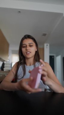 Modern bir evde oturan genç bir kadın pembe bir akıllı telefon sergiliyor, yaşam tarzını ve teknolojisini somutlaştırıyor.