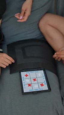 İki kişi tablet üzerinde TicTacToe oynuyor, evde rahat vakit geçiriyorlar, rekabetçi ama eğlenceli bir oyun ile bağ kuruyorlar.