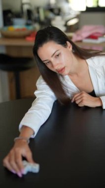 Beyaz gömlekli odaklanmış bir kadın, bir bulmaca oyunu oynuyor, modern bir evde siyah bir masada oturuyor..