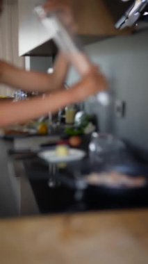 Modern bir mutfak sahnesi, yemek aletleri ve malzemelerle hareket halindeki elleri yakalıyor.