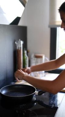 Kablosuz kulaklıklı genç bir kadın modern bir mutfakta yemek pişiriyor, teknolojiyi kullanıyor ve sağlıklı bir yemek hazırlıyor.