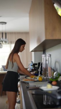 Genç bir kadın modern bir mutfakta doğal ışıkla yemek pişiriyor, taze malzemelerle yemek hazırlıyor..
