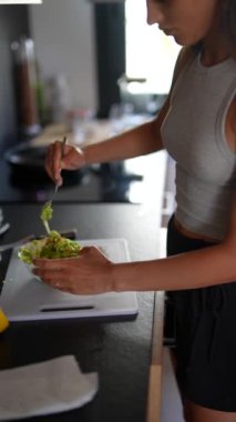 Bir kadın, doğal ışıkla dolu şık bir mutfakta besleyici yeşil bir salata yapıyor.