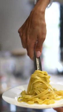 Fettuccine makarnası beyaz bir tabakta servis ediliyor, özellikle de elinde çatal bıçak tutarken..