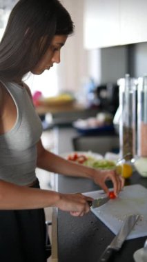 Genç bir kadın, sağlıklı bir yemek hazırlarken mutfak malzemeleriyle çevrili modern bir mutfakta sebze doğruyor.