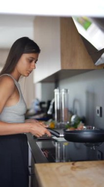 Modern bir mutfakta, genç bir kadın lezzetli ve sağlıklı bir yemek için indüksiyon sobasında taze malzemelerle yemek pişirir.
