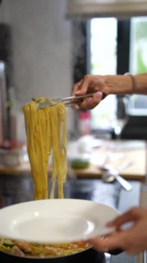 Mutfakta, bir aşçı yemek için bir tabak lezzetli spagetti servis etmek için maşa kullanıyor.