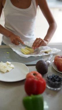 Bir insan mutfak tezgahında, sebze ve meyvelerle çevrili bir peynir hazırlıyor, taze ve sağlıklı bir yemek yapıyor.