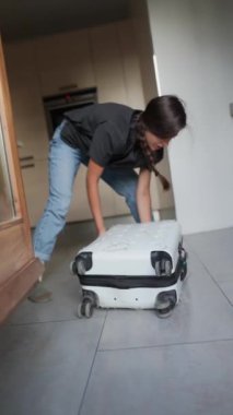 Çağdaş bir evde bavul hazırlarken beyaz bavulu kapatan kişi yolculuk için hazırlanıyor..