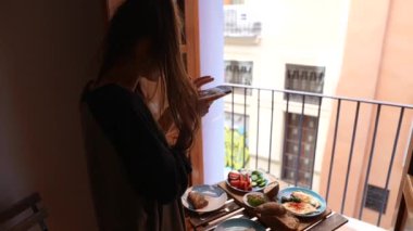 Bir kadın, bir balkonda kahvaltısını çekiyordu. Şehir manzarası manzaralı bir manzaraya karşıydı..