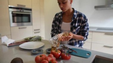 Moda mutfağında, genç bir bayan organik sebzeler ve malzemelerle taze ve besleyici bir yemek hazırlıyor.