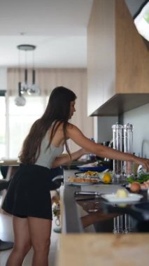 Modern bir mutfakta yemek hazırlayan kadın sohbete dalmış. Tezgahta taze malzemeler var..