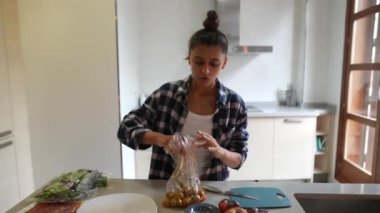Genç bir kadın, modern bir mutfakta taze marul, domates ve canlı sebzelerle sağlıklı salata yapıyor.