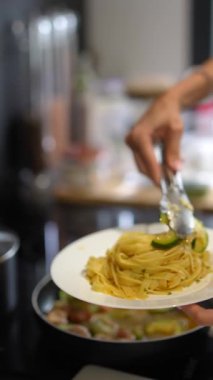 Şef, modern bir mutfak ortamında vurgulanmış beyaz bir tabakta güzel pişirilmiş makarna servis ediyor..