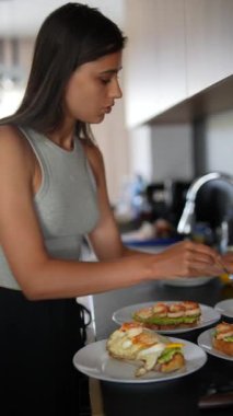Genç bayan, günümüzün mutfağında haşlanmış yumurtalarla lezzetli avokado tostlarını dikkatlice hazırlıyor..