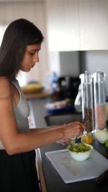 Genç bir kadın, modern bir mutfakta taze malzemelerle yemek pişiriyor. Mutfak yaratıcılığı ve sağlıklı yaşam sunuyor.