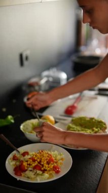 Modern bir mutfakta mısır, marul ve domates gibi taze malzemelerle sağlıklı bir salata hazırlayan kişi..