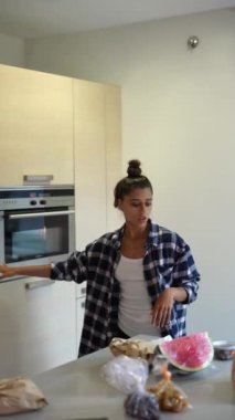 Günlük kıyafetli bir kadın hafta sonu rutininin bir parçası olarak fırının yanındaki modern bir mutfakta kurabiye pişiriyor.