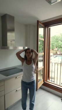 Modern bir mutfakta, parlak güneş ışığı odayı açık bir pencereden doldururken tek eliyle yüzünü kapatan bir kadın.