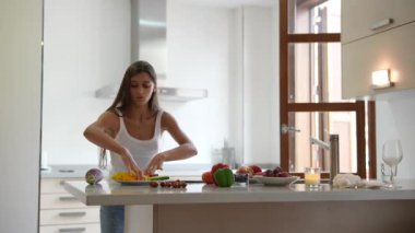 Modern bir mutfakta taze malzemeler kullanarak yemek pişiren ve yemek hazırlarken akıllı telefonunu kontrol eden bir kadın..