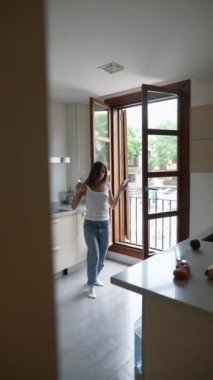 Bir kadın modern bir mutfakta sabah güneşinin tadını çıkarır. Pencere kenarında kahvesini yudumlar, rahat bir ortam yaratır.