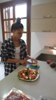 Modern bir mutfakta, kareli gömlekli genç bir kadın taze salata hazırlamak için malzemeleri doğruyor.