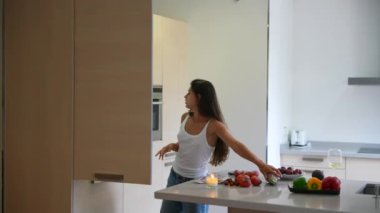 Beyaz kolsuz tişörtlü bir kadın tezgahta taze sebze ve meyvelerle mutfak dolabını açıyor..