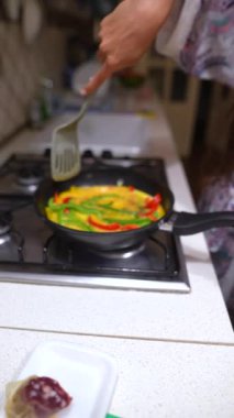 Bir insan mutfaktaki sobanın üstünde renkli ve sağlıklı sebzeli omlet pişirir ve dengeli bir yemek sunar.