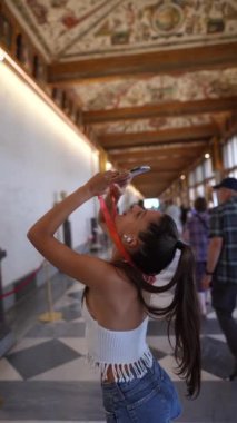 Genç bir kadın bir müze koridorunda selfie çubuğu kullanıyor, anları yakalıyor ve sanat eserlerini ve kültürlerini keşfediyor.