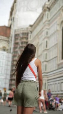 Kahverengi saçlı esmer bir kadın güneşli bir günde bir Avrupa şehrinin tarihsel mimarisini keşfediyor.