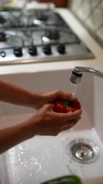 Mutfak lavabosunda arka planda sobayla akan suyun altında kırmızı biber yıkayan biri..