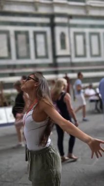 Mutlu bir kadın şehrin heyecanından zevk alıyor kollarını açmış, insanlarla çevrili ve anı kucaklıyor.